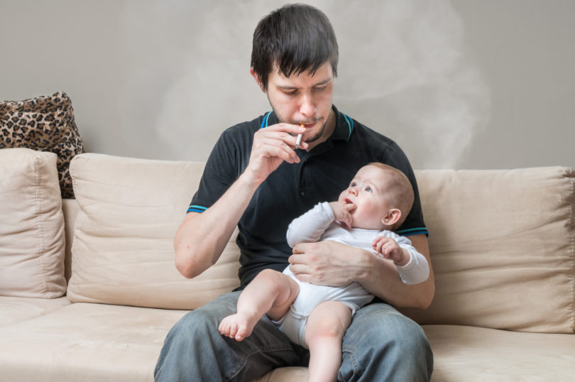 Ein Vater der Zigaretten raucht und dabei sein Baby im Arm hält